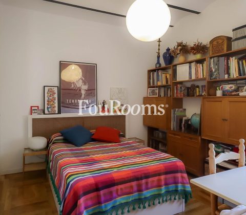 dormitorio con cama con colcha de colores y estantería con libros