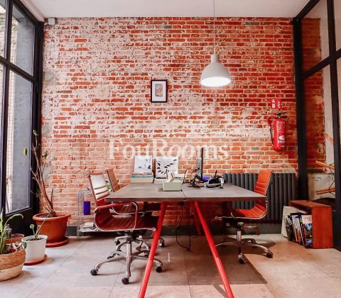 interior de despacho con ventanales, mesa con sillas y pared de ladrillos
