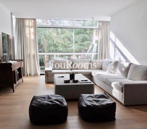 salón con sofá esquinero blanco y dos pufs marrones y ventanal