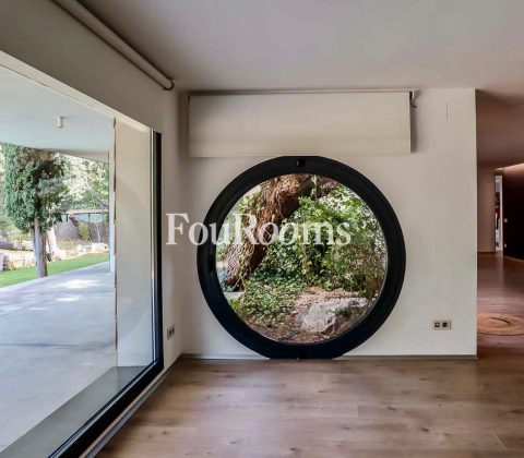 vista del jardín desde el interior con ventanal rectangular y ventanal redondo